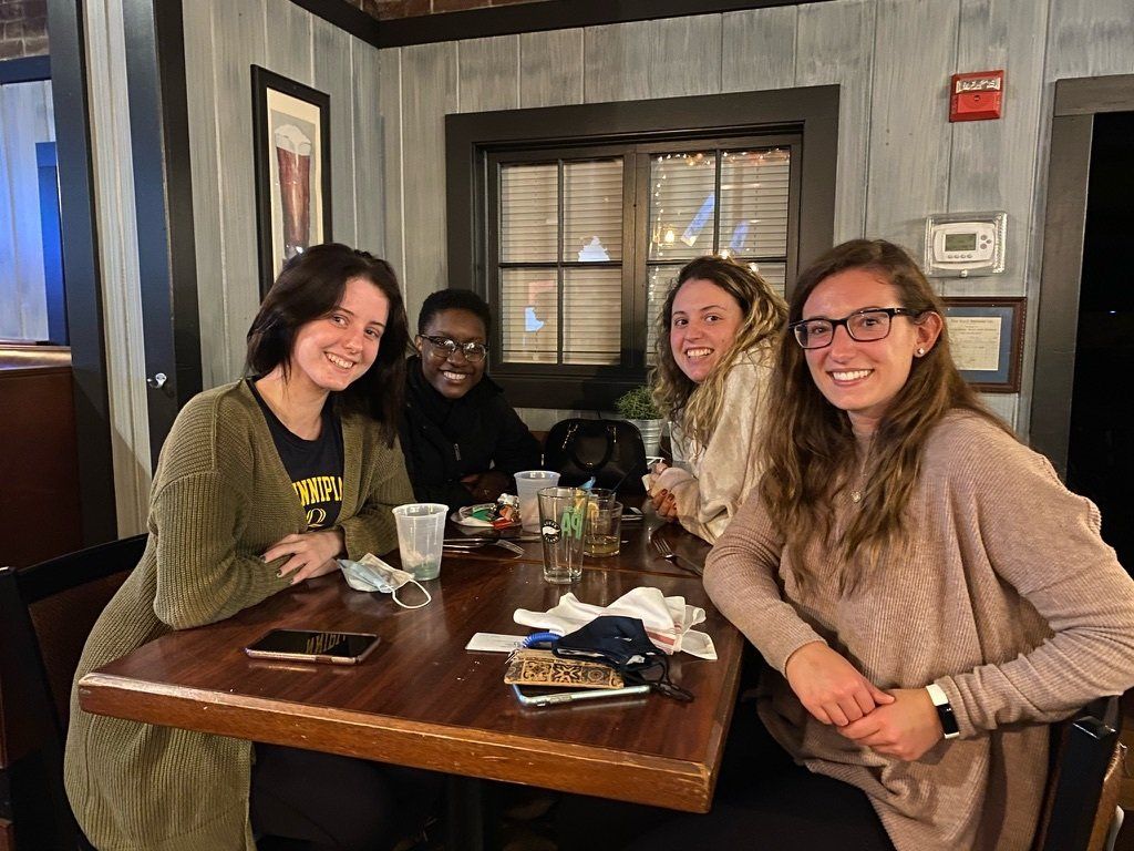 Four people at a table in a dimly lit restaurant, smiling at the camera. Drinks and food on the table.