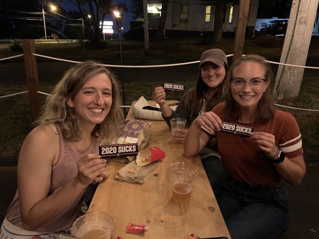 Three smiling people at an outdoor table, holding signs that say 