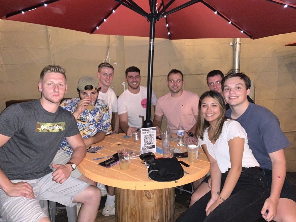 Group of people smiling at an outdoor table under a red umbrella.