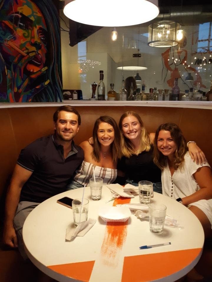 Four people seated at a round table in a restaurant booth, smiling. There's artwork in the background.