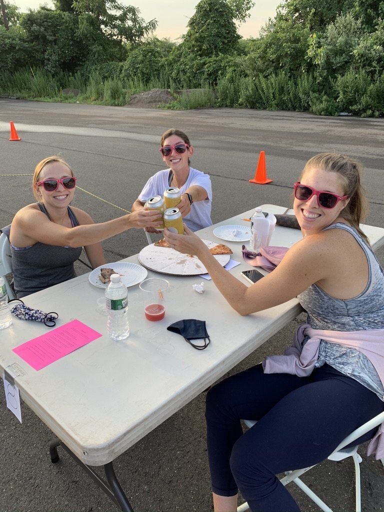 Three people toast drinks outdoors at a table, all wearing pink sunglasses.