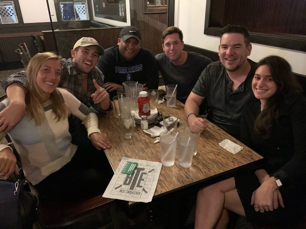 Six people seated at a table in a restaurant; smiling and looking at the camera.