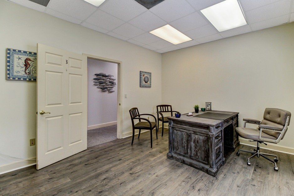 Small office with desk, chairs, white walls, and open doorway on wood-look flooring