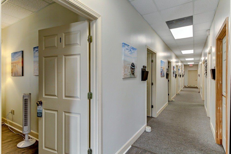 Open office hallway with white walls, carpet, doors, and ceiling lights stretching into the distance