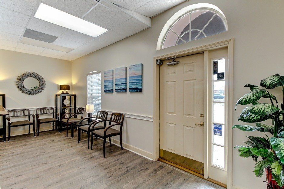 Bright waiting room with chairs, wall art, lamp, wood flooring, and a beige door with arched window.