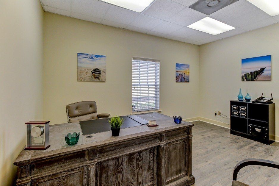 Office with wooden desk, beige walls, window blinds, wall art, and a black cabinet with shelves.