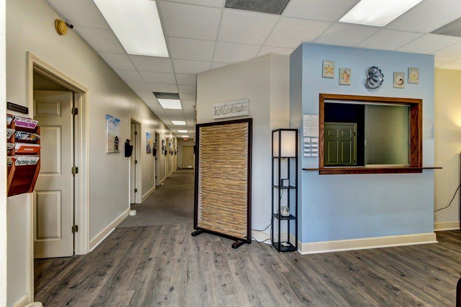 Bright office hallway with gray flooring, light blue walls, a reception window, and stone accent divider