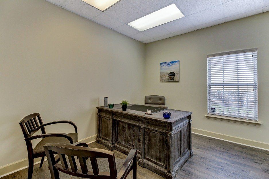 Small office with two wooden chairs, a desk, wall art, and a window with blinds.
