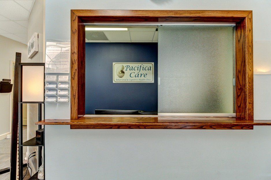 Reception window with wooden frame and frosted glass in a hallway, sign on blue wall inside.