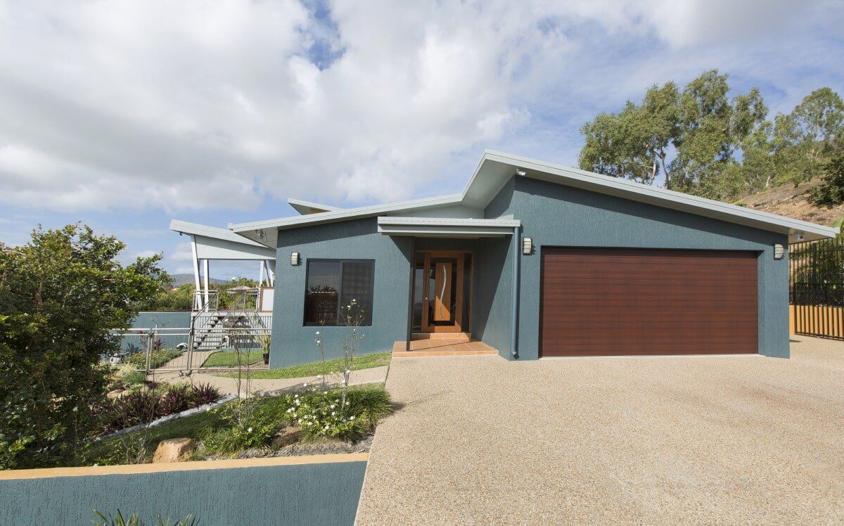 Blue house with brown garage door and driveway against a cloudy sky.