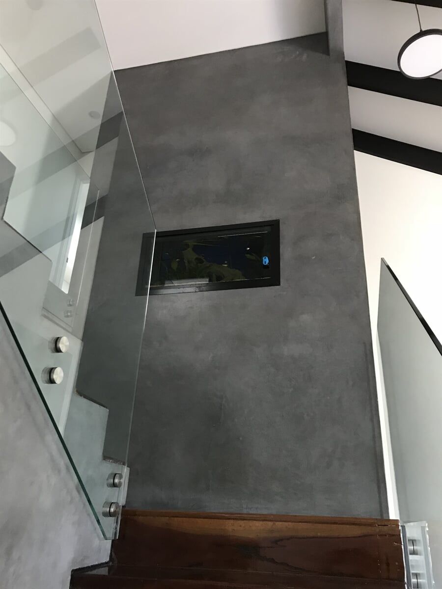 Gray textured wall with a mounted television next to a glass staircase.