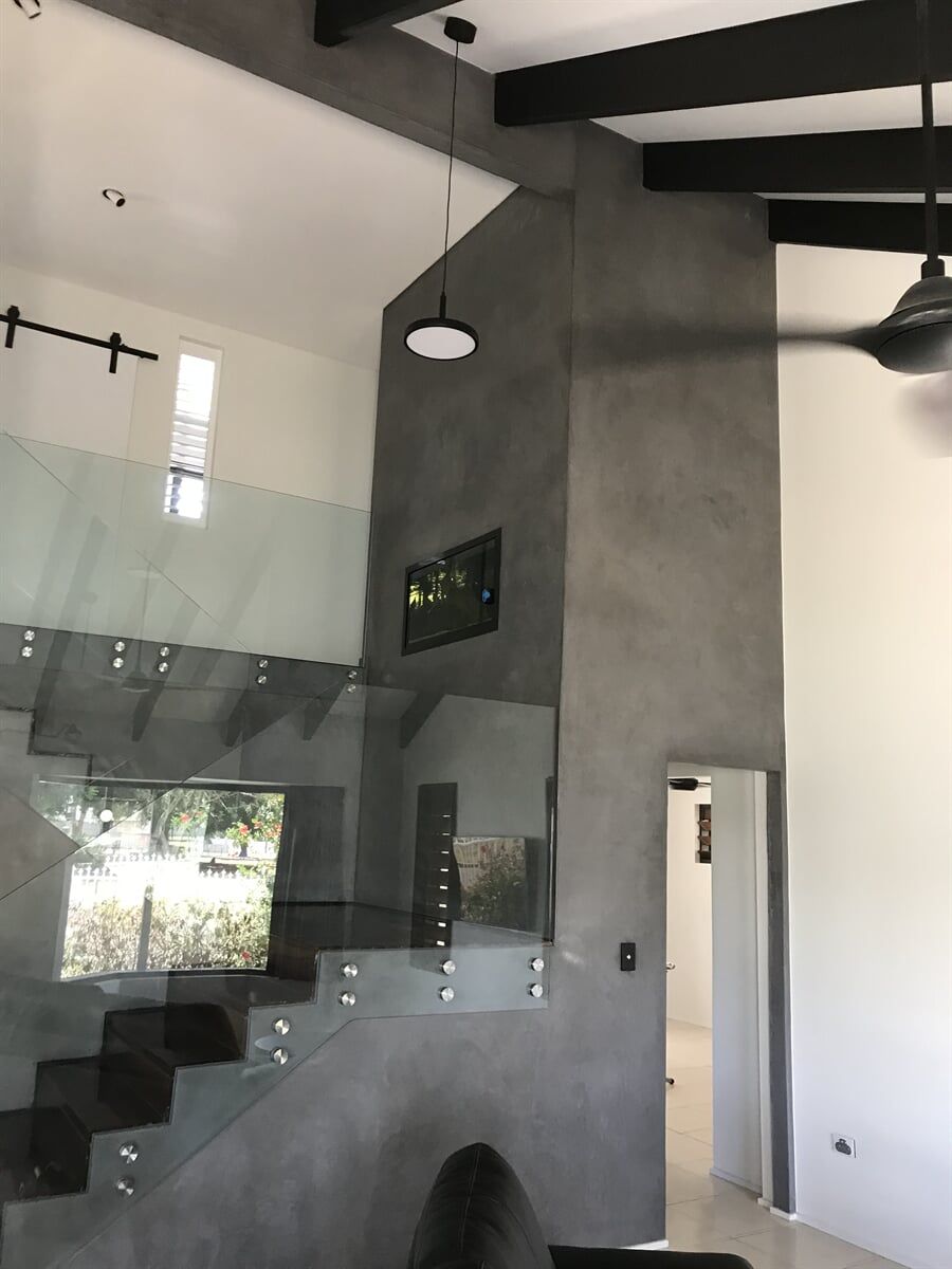 Modern interior with glass staircase, gray accent wall, black beams, and a hanging light.