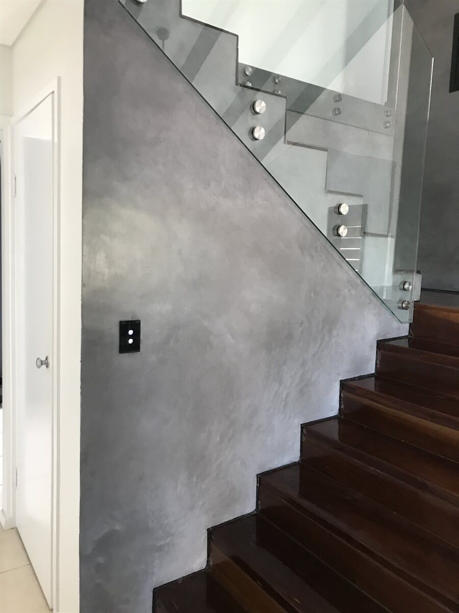 Gray textured wall alongside wooden staircase with glass railing.