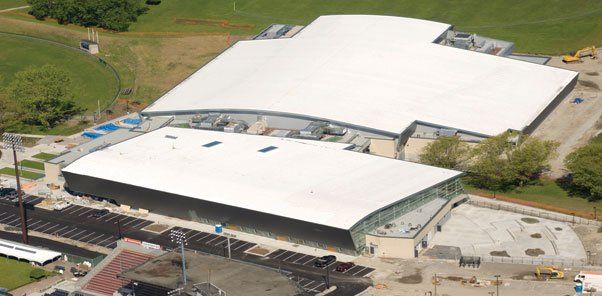 An aerial view of a large building with a white roof surrounded by trees.