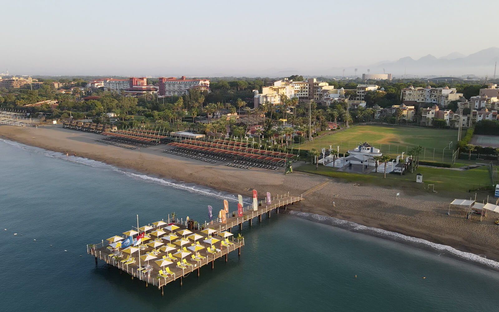 Eine Luftaufnahme eines Strandes mit einem Pier und Sonnenschirmen.
