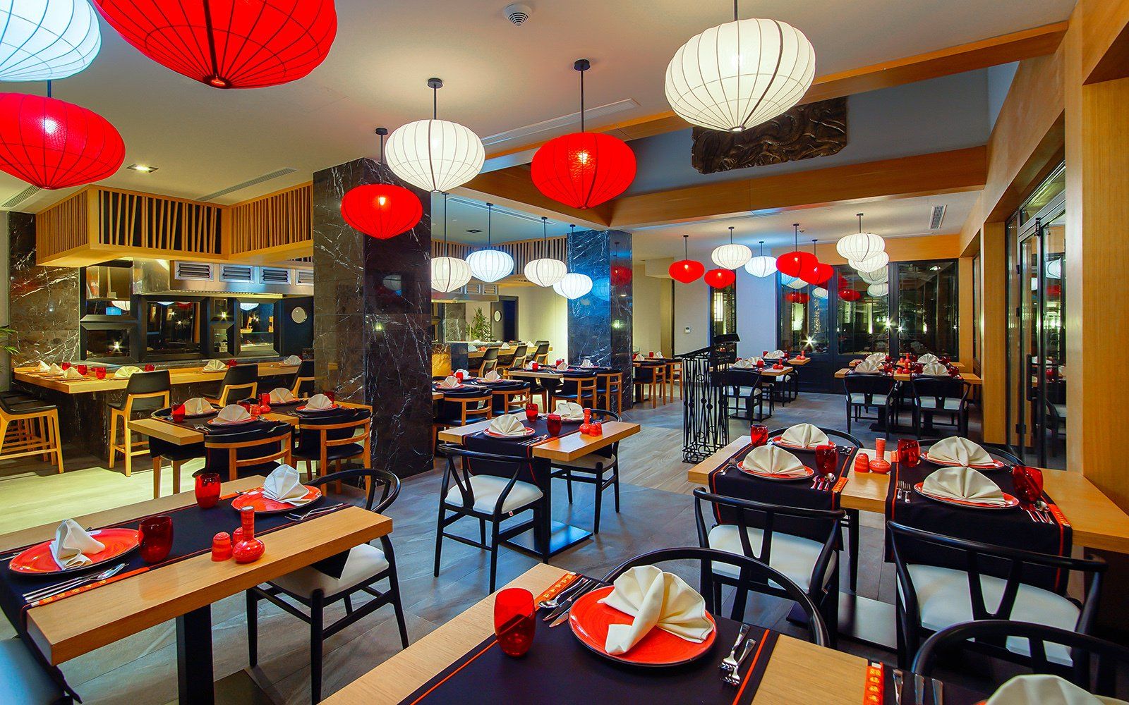 A restaurant with tables and chairs and red lanterns hanging from the ceiling.