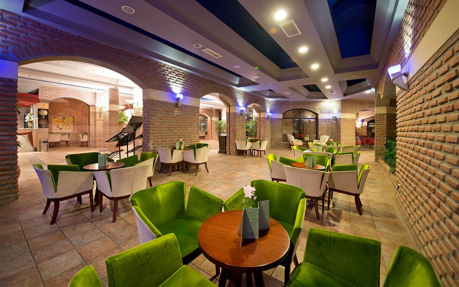 Ein Restaurant mit grünen Stühlen und Tischen und einer Backsteinwand.
