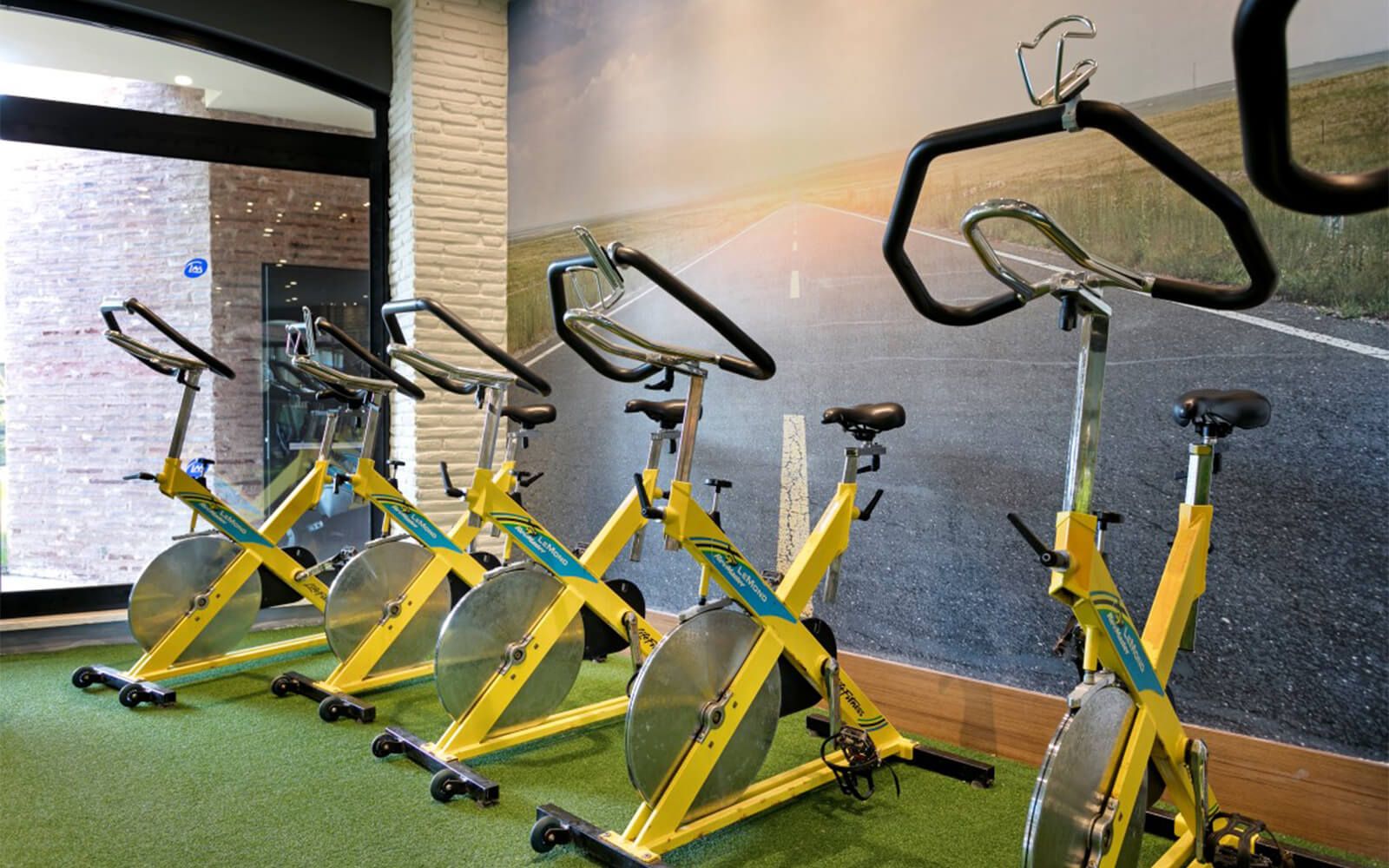 In einem Fitnessstudio stehen mehrere gelbe Heimtrainer in einer Reihe.