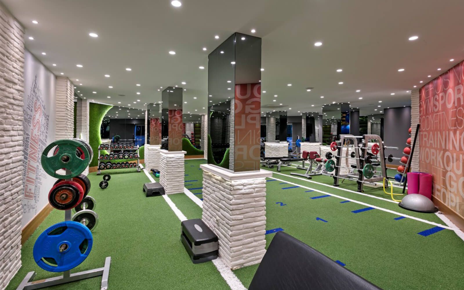 Ein großer Fitnessraum mit vielen Geräten und einem grünen Teppich.