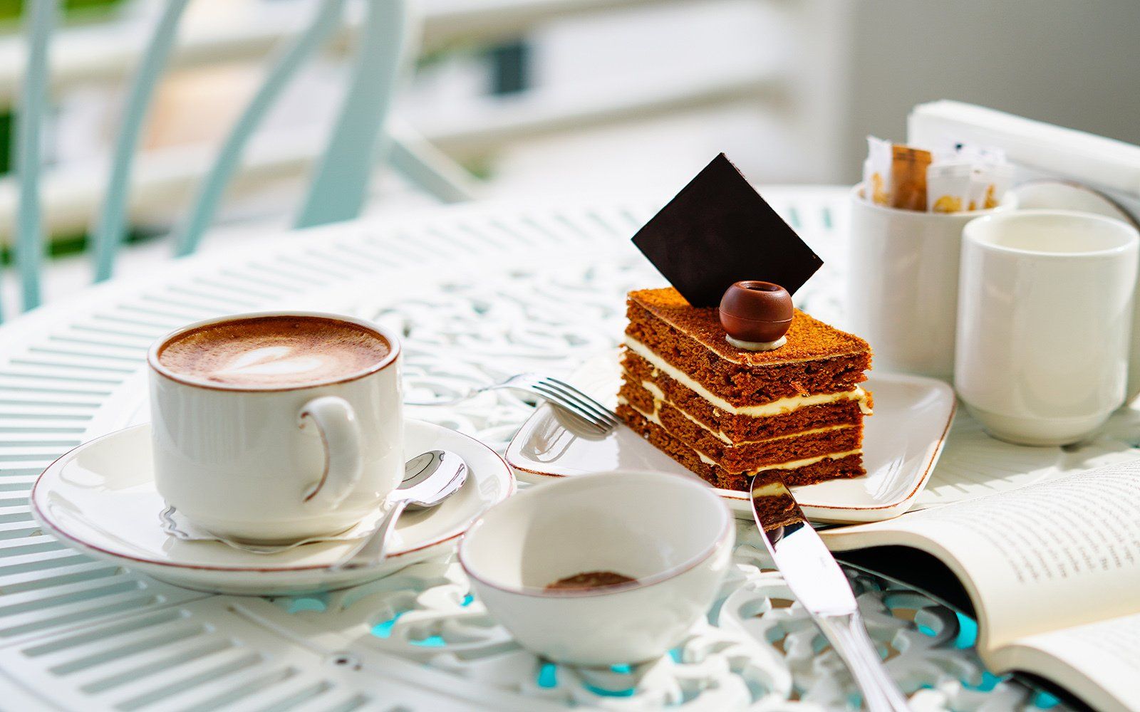 A table with a cup of coffee and a piece of cake on it.