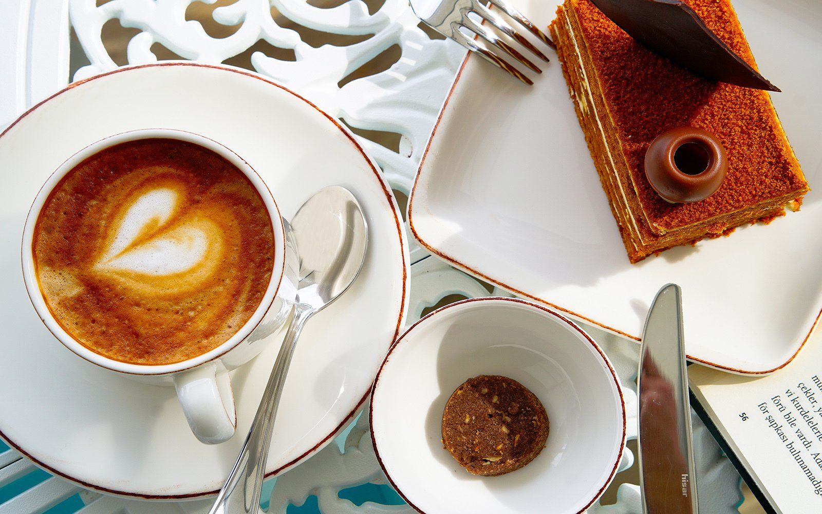 A cup of coffee on a saucer next to a piece of cake