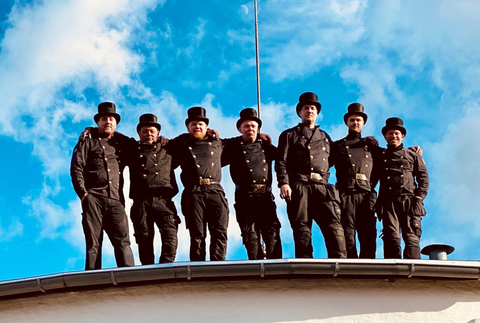 En gruppe skorstensfejere stiller op til et billede på toppen af ​​en bygning.
