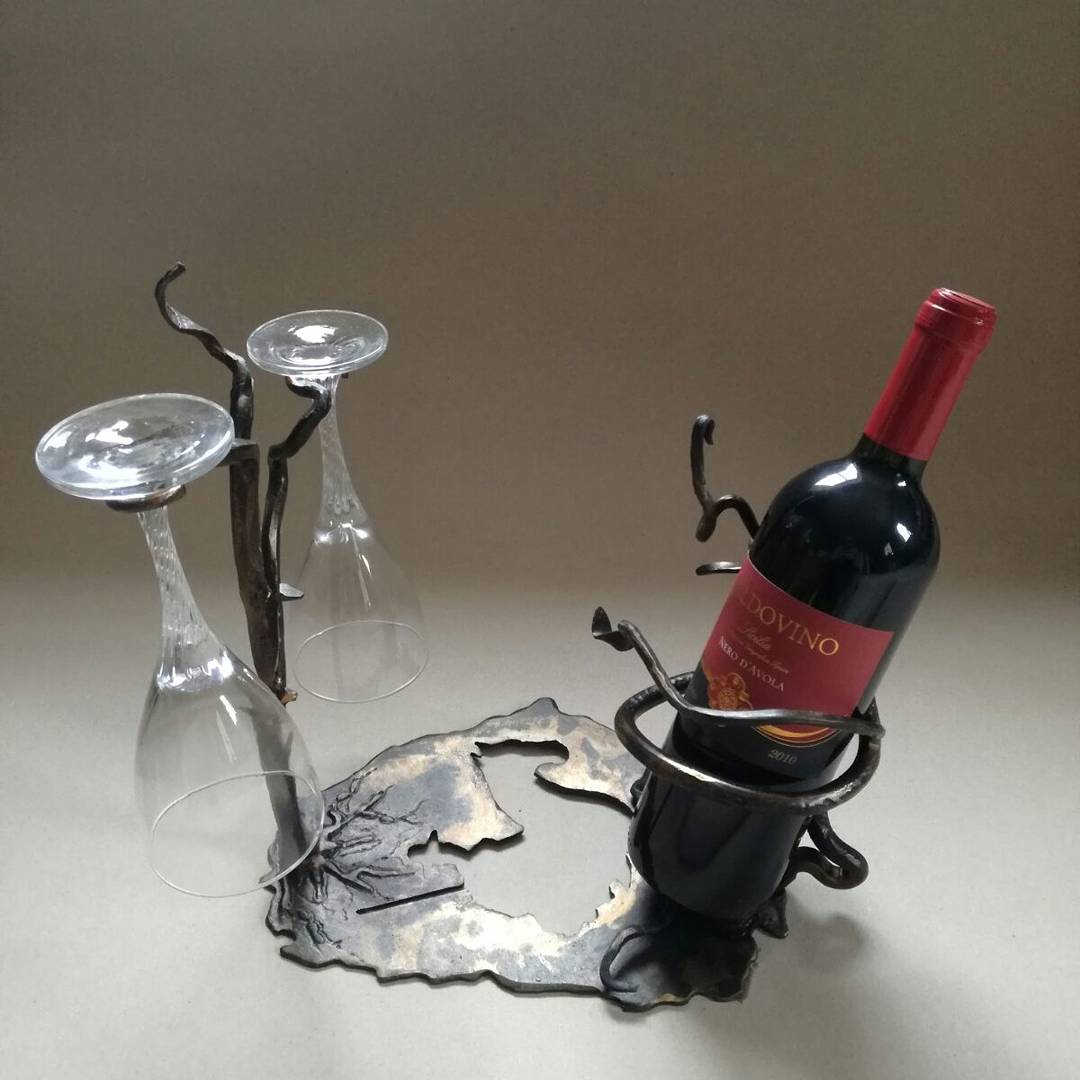 Una bottiglia di vino in un supporto di metallo nero accanto a due calici da vino capovolti su un vassoio decorativo.