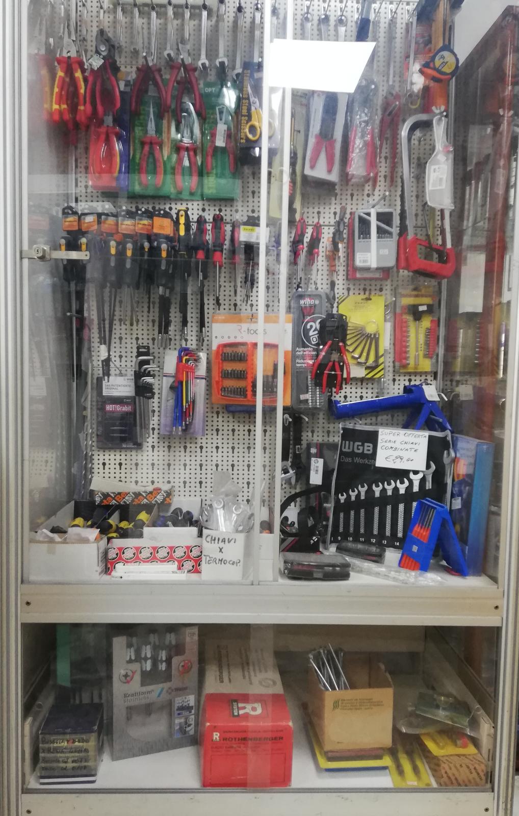 Vetrina di un negozio di ferramenta con un assortimento di utensili manuali in una teca di vetro, tra cui pinze, chiavi inglesi e articoli confezionati.