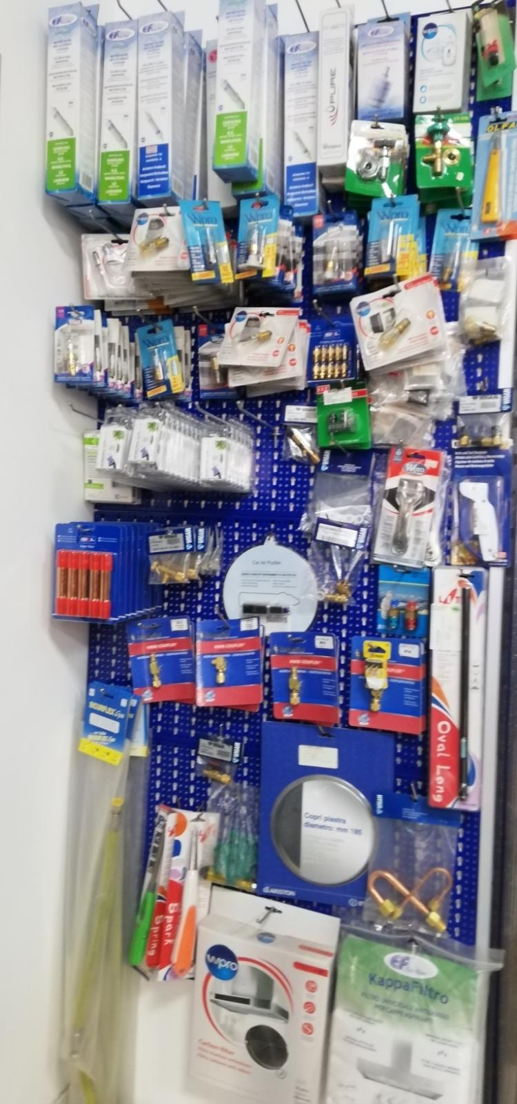Esposizione in un negozio di ferramenta di cavi, adattatori e accessori elettronici confezionati di vario tipo, su una parete attrezzata con pannelli forati.