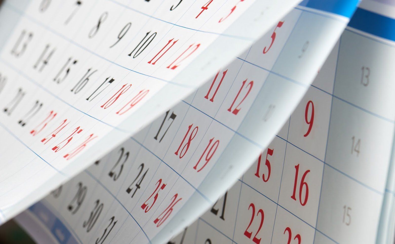 Close-up of a calendar with pages flipping; red and black numbers.