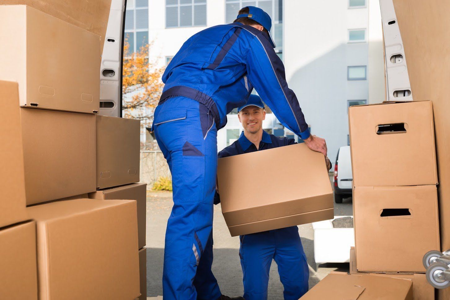 Two movers in blue uniforms loading cardboard boxes into a van.