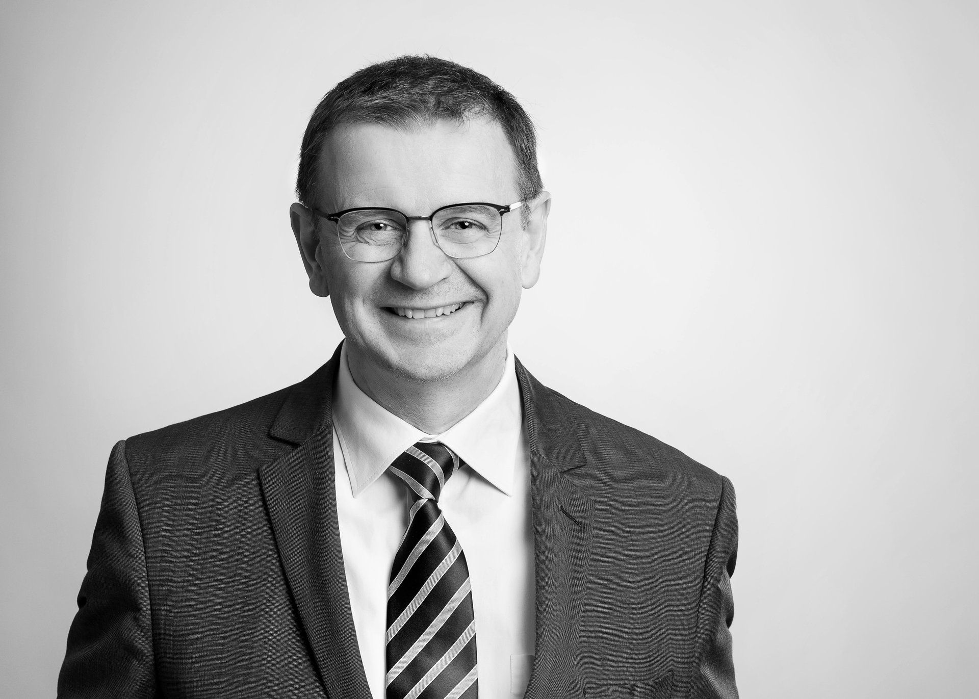 Auf einem Schwarzweißfoto lächelt ein Mann in Anzug und Krawatte.