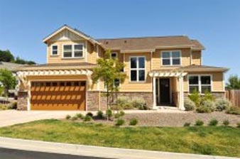 Two-story yellow house with brown garage door and trim, small yard, blue sky.