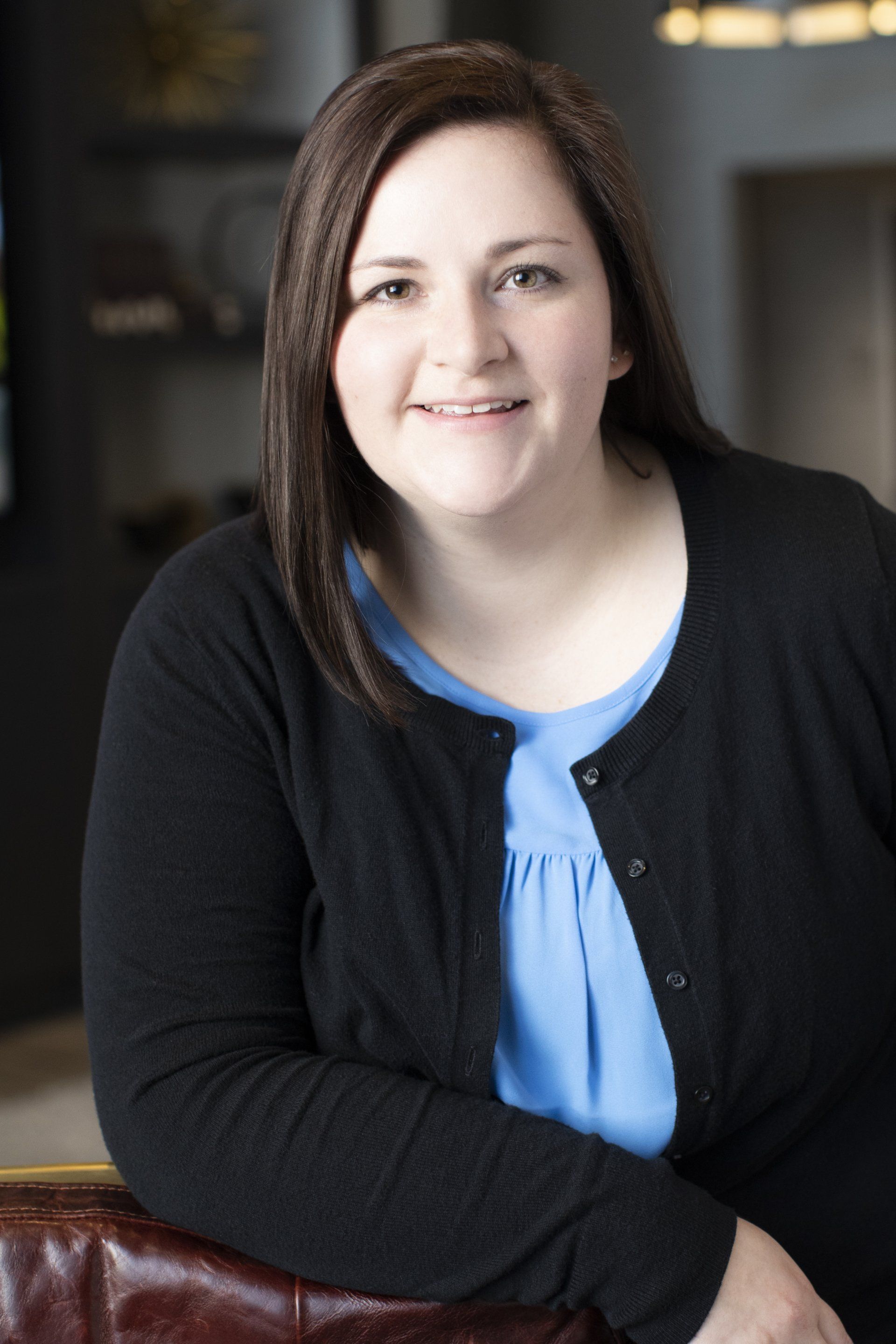 A woman wearing a black cardigan and a blue shirt is smiling for the camera.