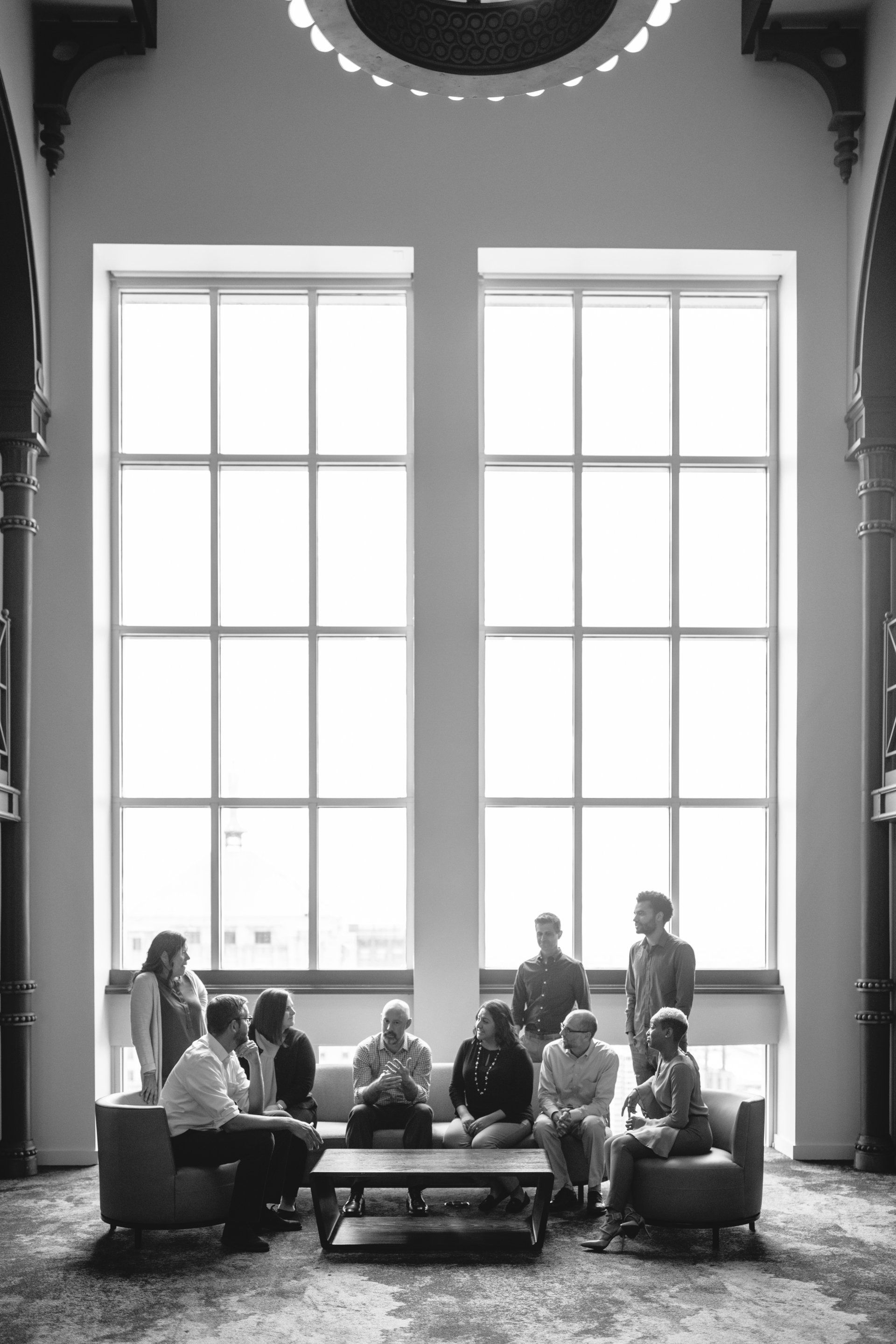 A group of people are sitting around a table in front of a large window.