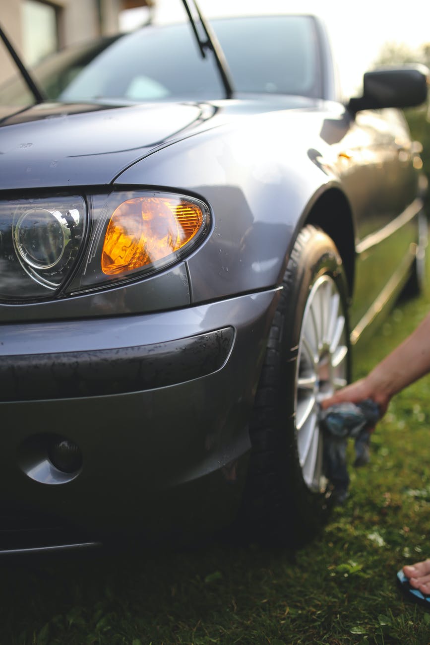 Grey car being washed; person cleaning a tire on a grassy lawn.