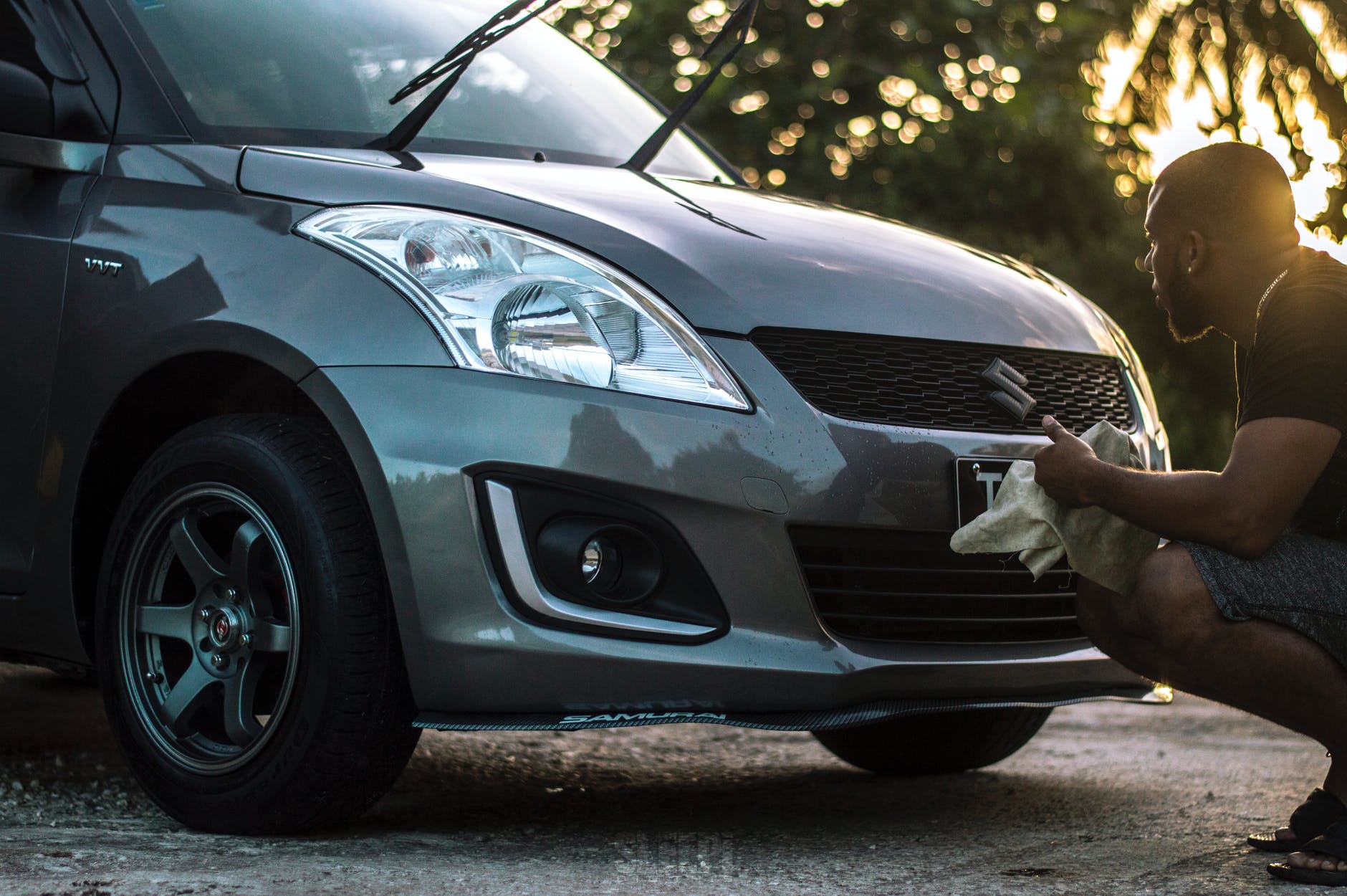 Man wiping the front of a gray car. Exterior shot, sunny day.