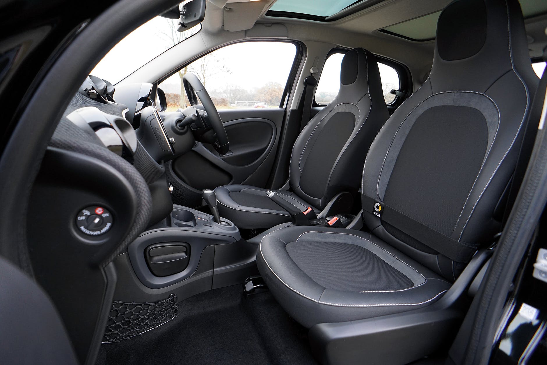 Interior of a black car with gray and black fabric seats; steering wheel, dashboard, and a sunroof are visible.