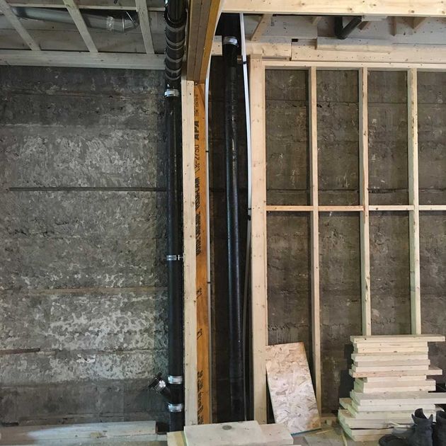 Black plumbing pipes in wooden frame, next to a concrete wall. Framing and lumber visible.