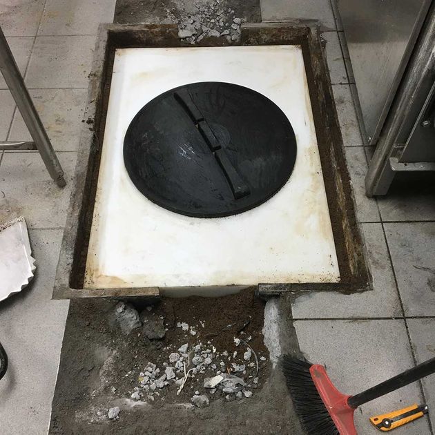 Black circular cover inside a recessed floor drain. Concrete repair in progress, with debris.