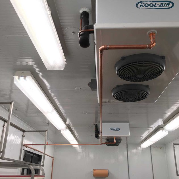 Ceiling of a refrigerated room with Kool-Air unit, copper pipes, fluorescent lights.