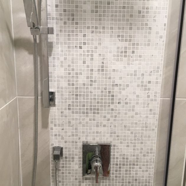 Shower with mosaic tile accent, silver showerhead, and faucet against neutral-colored tile walls.