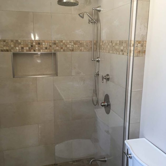 Shower stall with glass door, beige tile, and a mosaic tile accent strip.