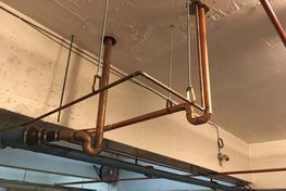Copper pipes suspended from a ceiling. Various joints and bends create an overhead plumbing system.