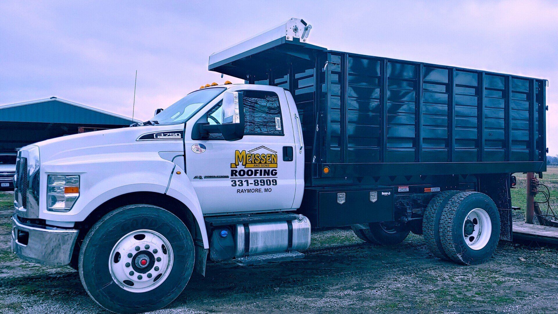 A white dump truck with a black bed is parked in a field.