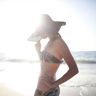 Silhouetted person in a sunhat and striped bikini standing by the ocean at sunset