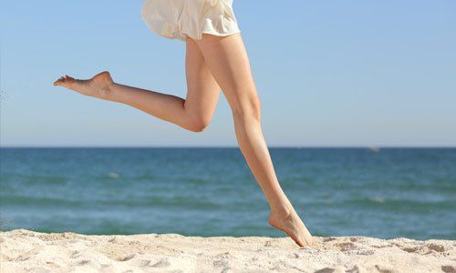 Person leaping barefoot on a sandy beach with the ocean in the background