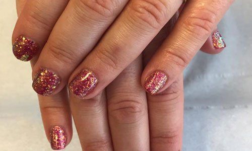 Hands with glittery pink and gold manicured nails resting together on a light surface