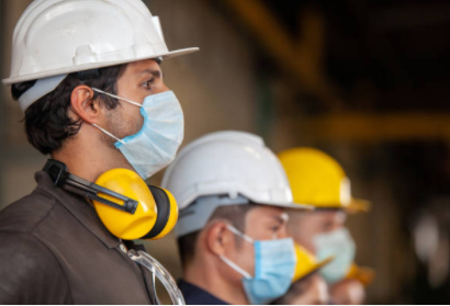 Construction workers wearing hard hats and face masks, standing in a row indoors.