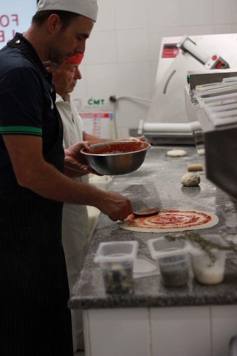 pizzaiolo guarnisce una pizza con pomodoro